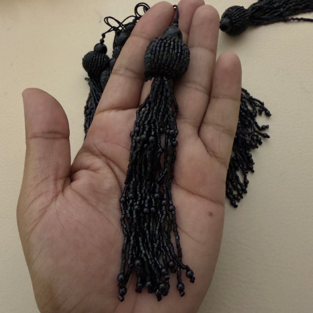 Black tassel held in a hand against a beige background
