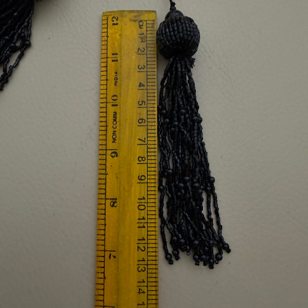 Black tassel next to a ruler on a white background