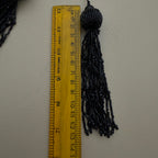 Black tassel next to a ruler on a white background