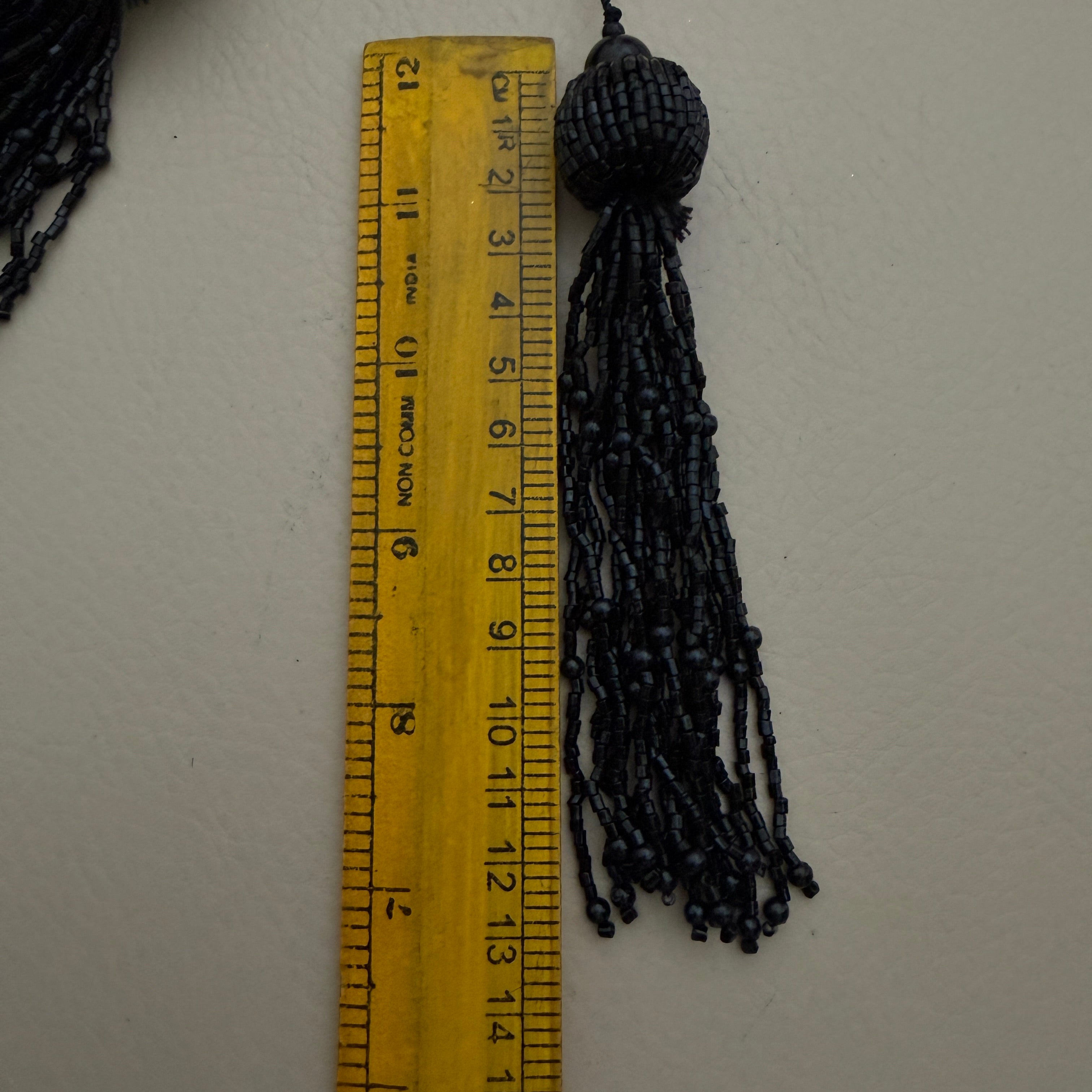 Black tassel next to a ruler on a white background