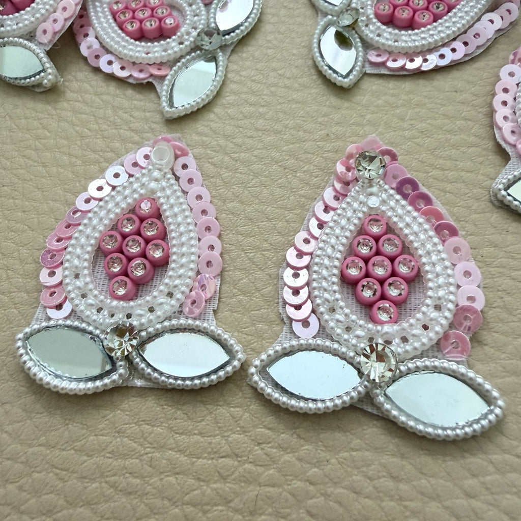 Close-up of pink teardrop patches with pearl-look bead borders and two leaf-shaped mirror accents