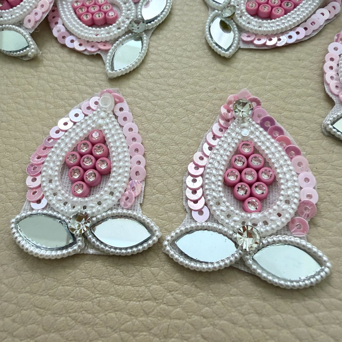 Close-up of pink teardrop patches with pearl-look bead borders and two leaf-shaped mirror accents