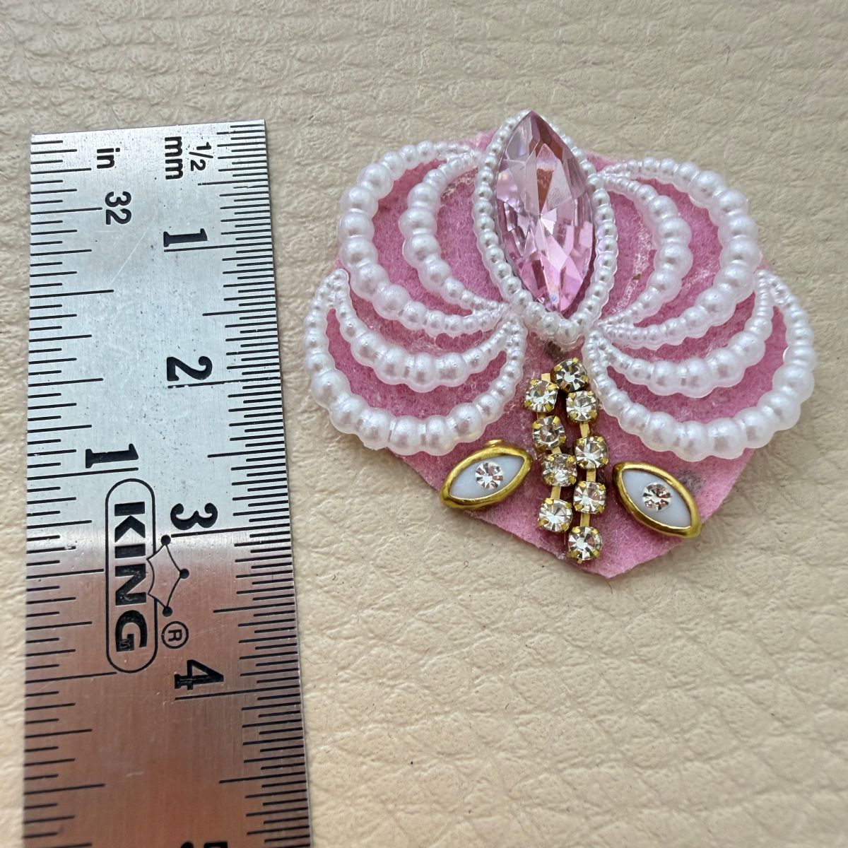 Pink pearl-effect and rhinestone fan patch beside a metric ruler for size reference