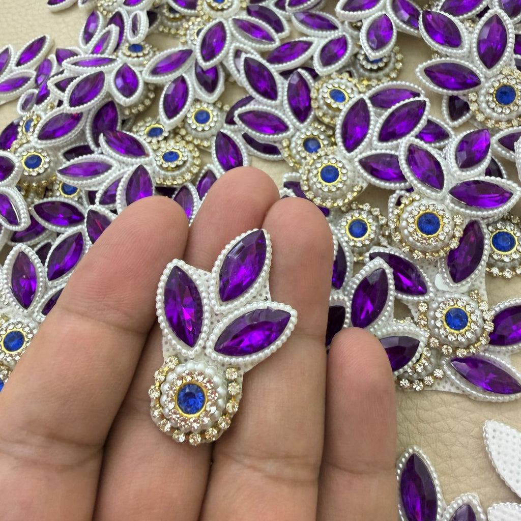 Close-up of two purple leaf patches with royal-blue stones, white pearl-look beads and gold-tone settings