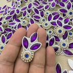 Close-up of two purple leaf patches with royal-blue stones, white pearl-look beads and gold-tone settings