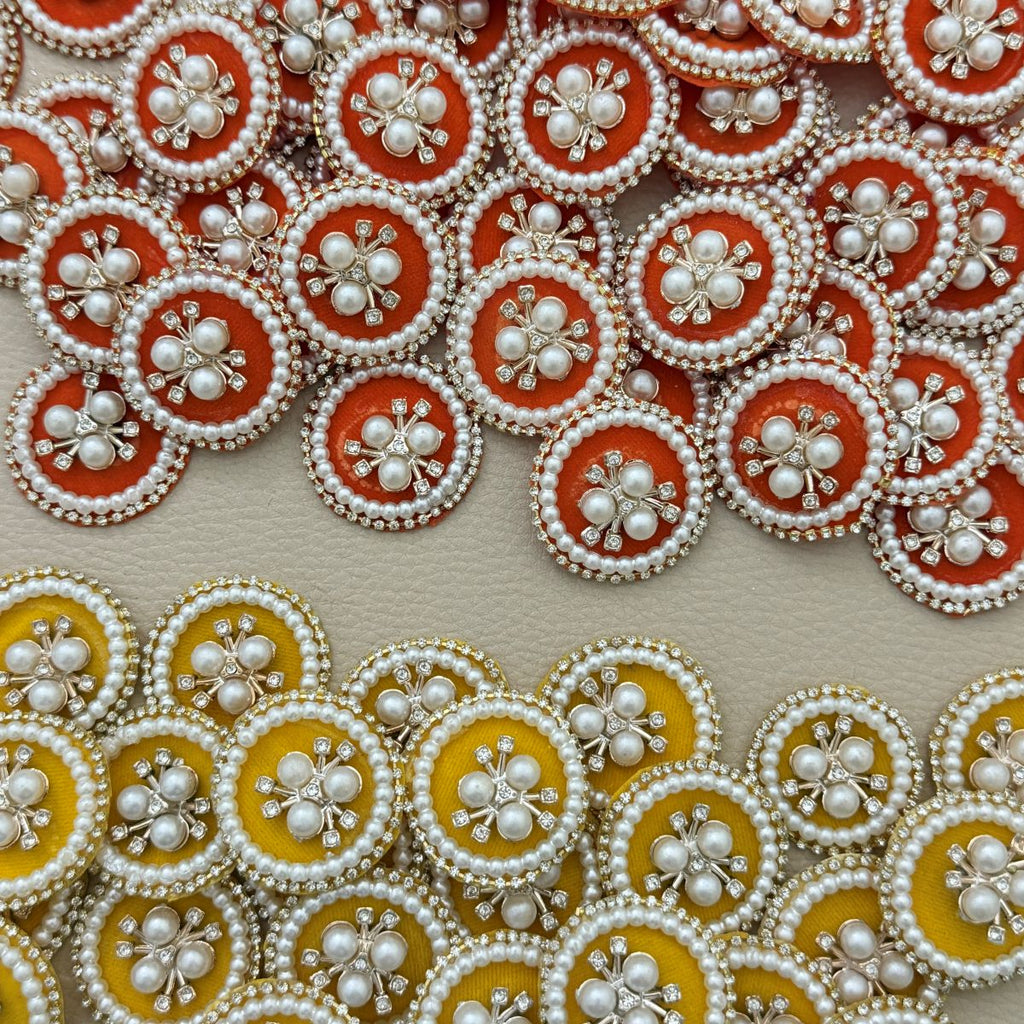 Yellow round pearl and rhinestone floral patch held in hand with orange patches behind