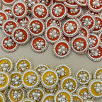 Yellow round pearl and rhinestone floral patch held in hand with orange patches behind