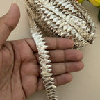 Gold decorative trim held between fingers against a neutral background