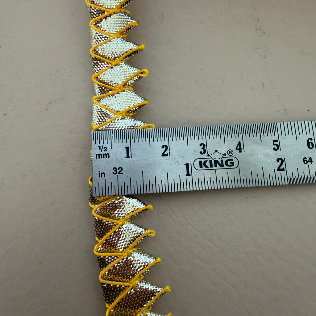 Decorative trim with gold and silver pattern on a gray background, measured by a King ruler.