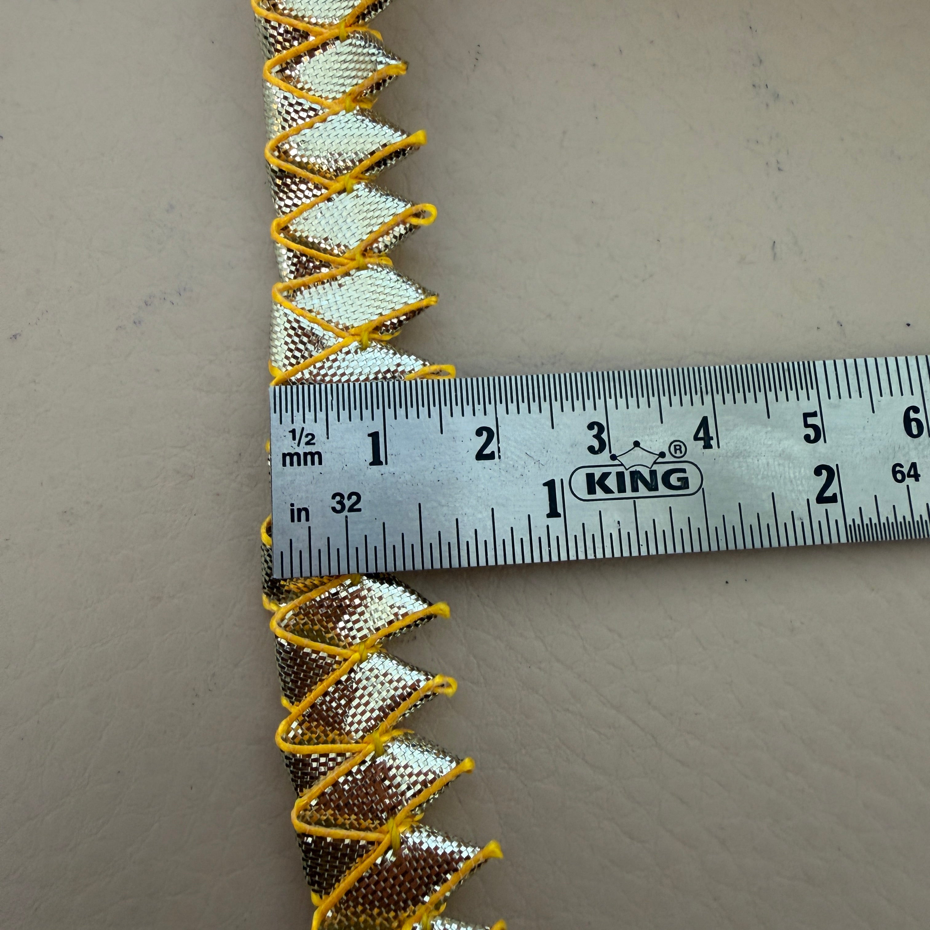 Decorative trim with gold and silver pattern on a gray background, measured by a King ruler.