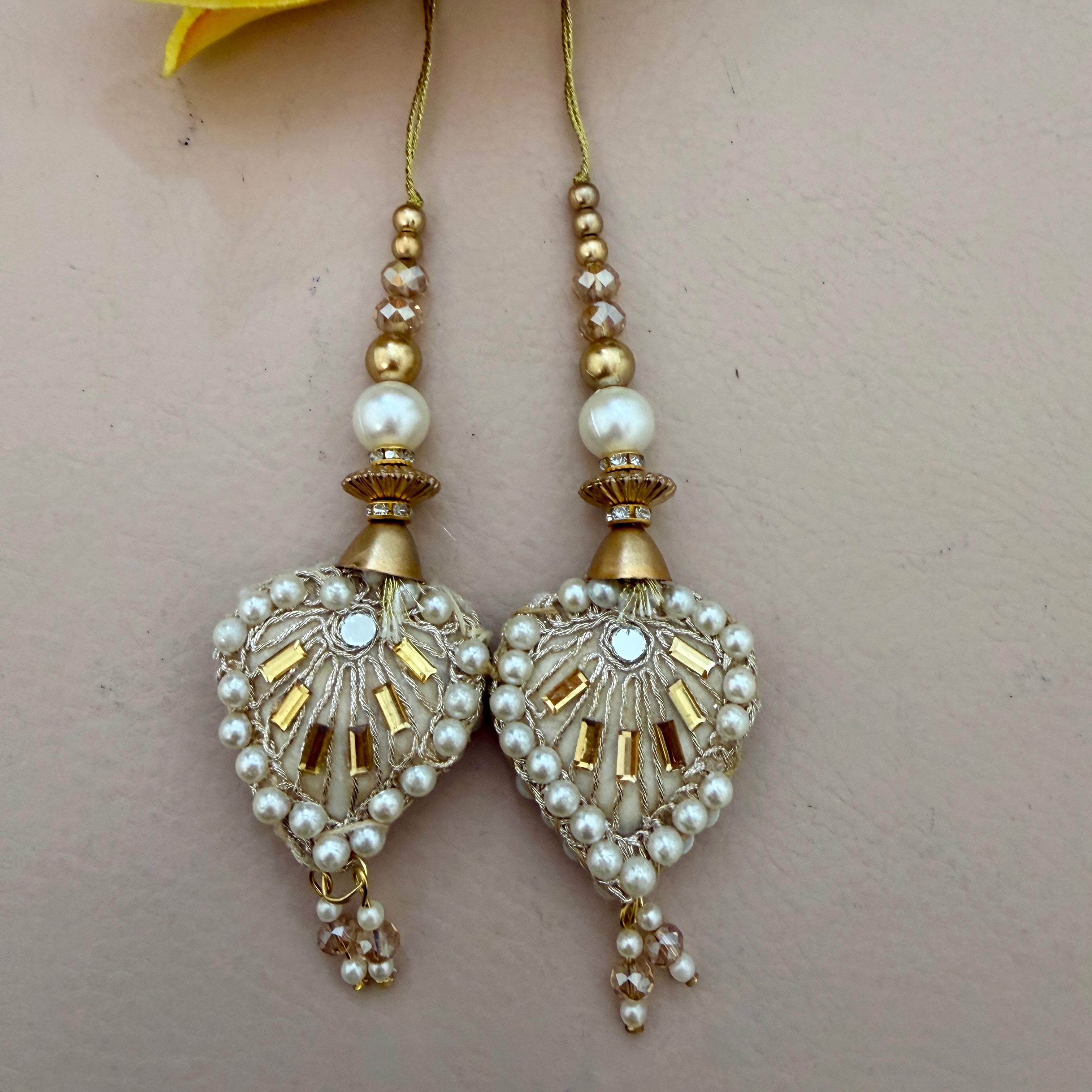 Decorative keychain with pearls and gold accents held in a hand, with yellow flowers in the background.