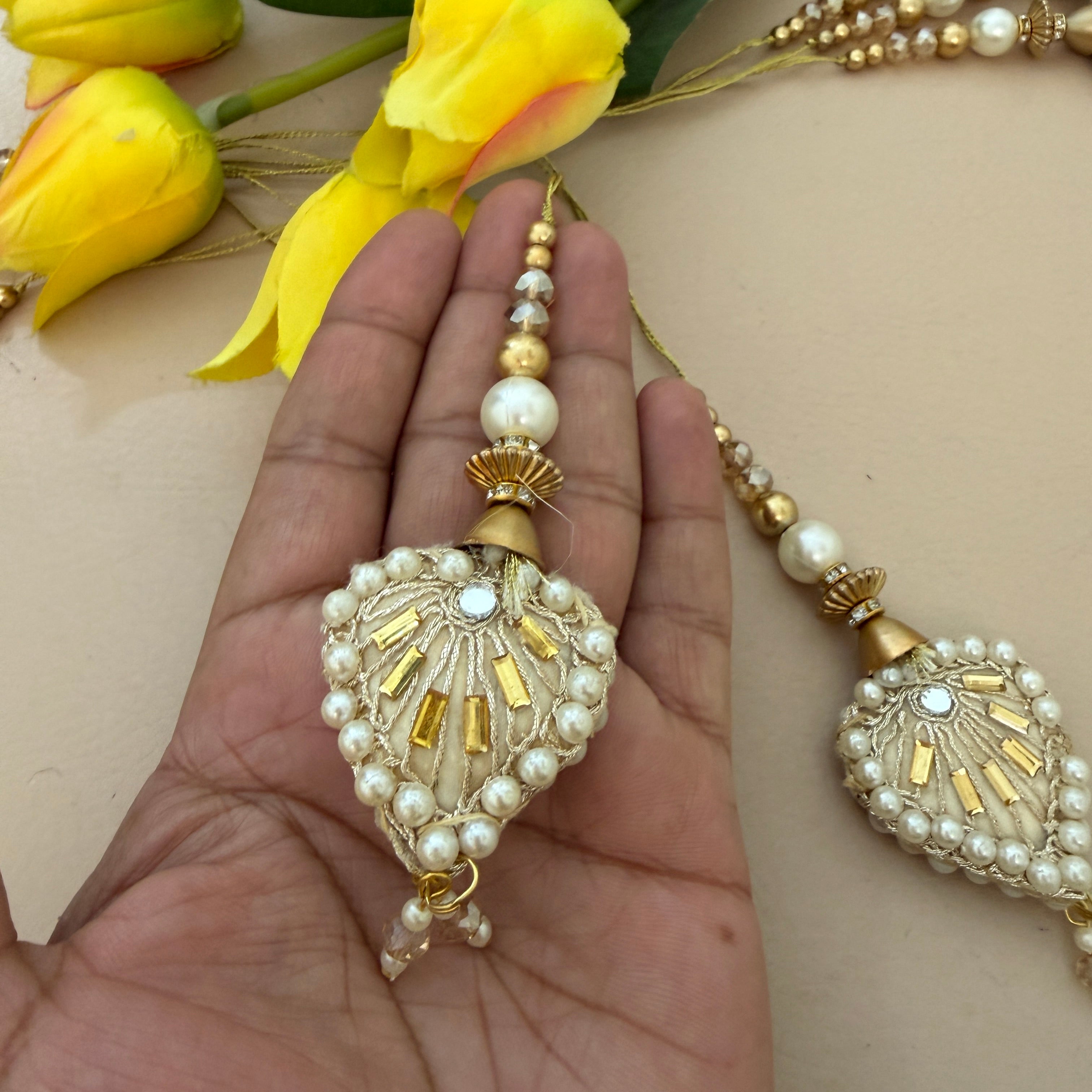 Decorative keychain with pearls and gold accents held in a hand, with yellow flowers in the background.