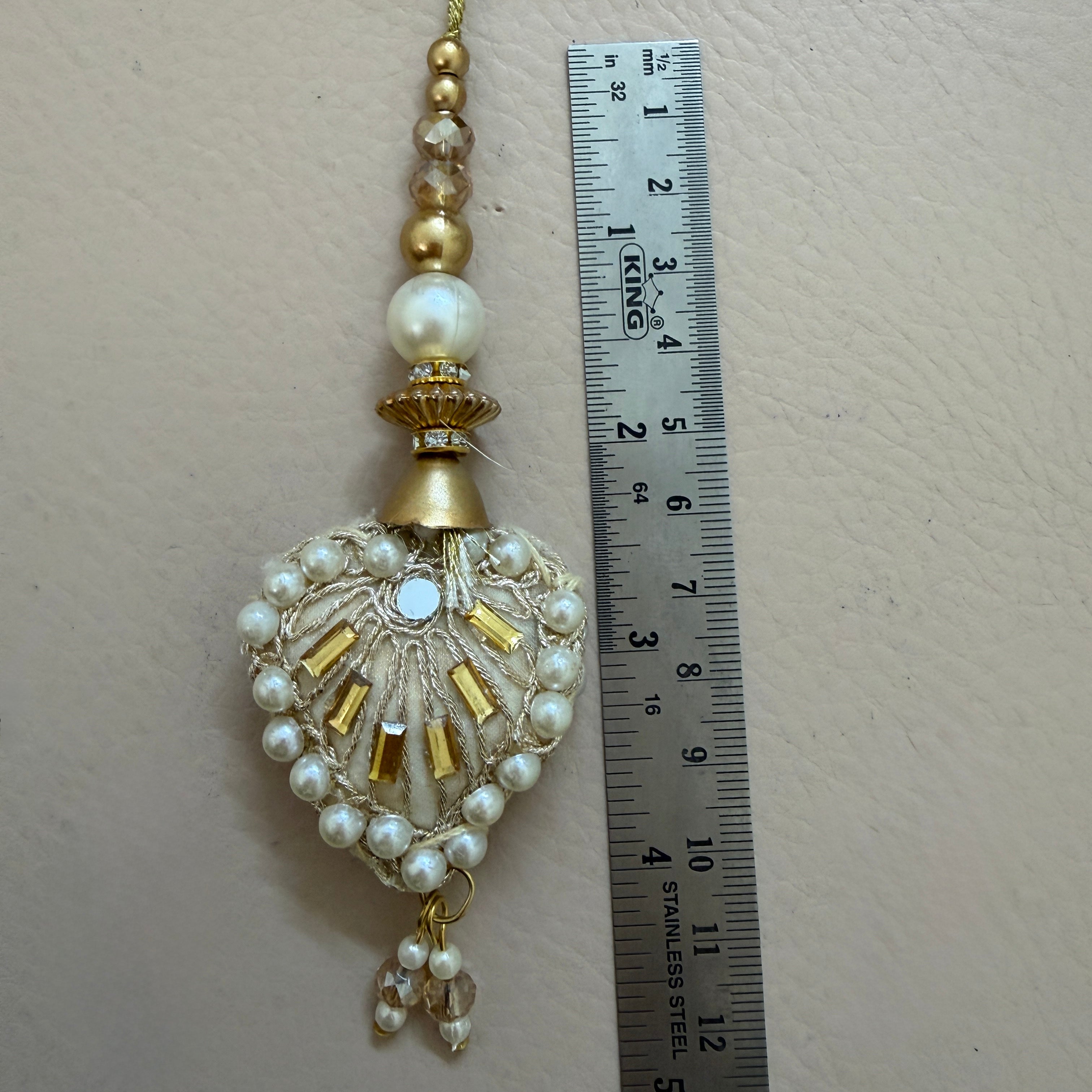 Decorative hanging ornament with pearls and beads next to a ruler for scale on a beige background