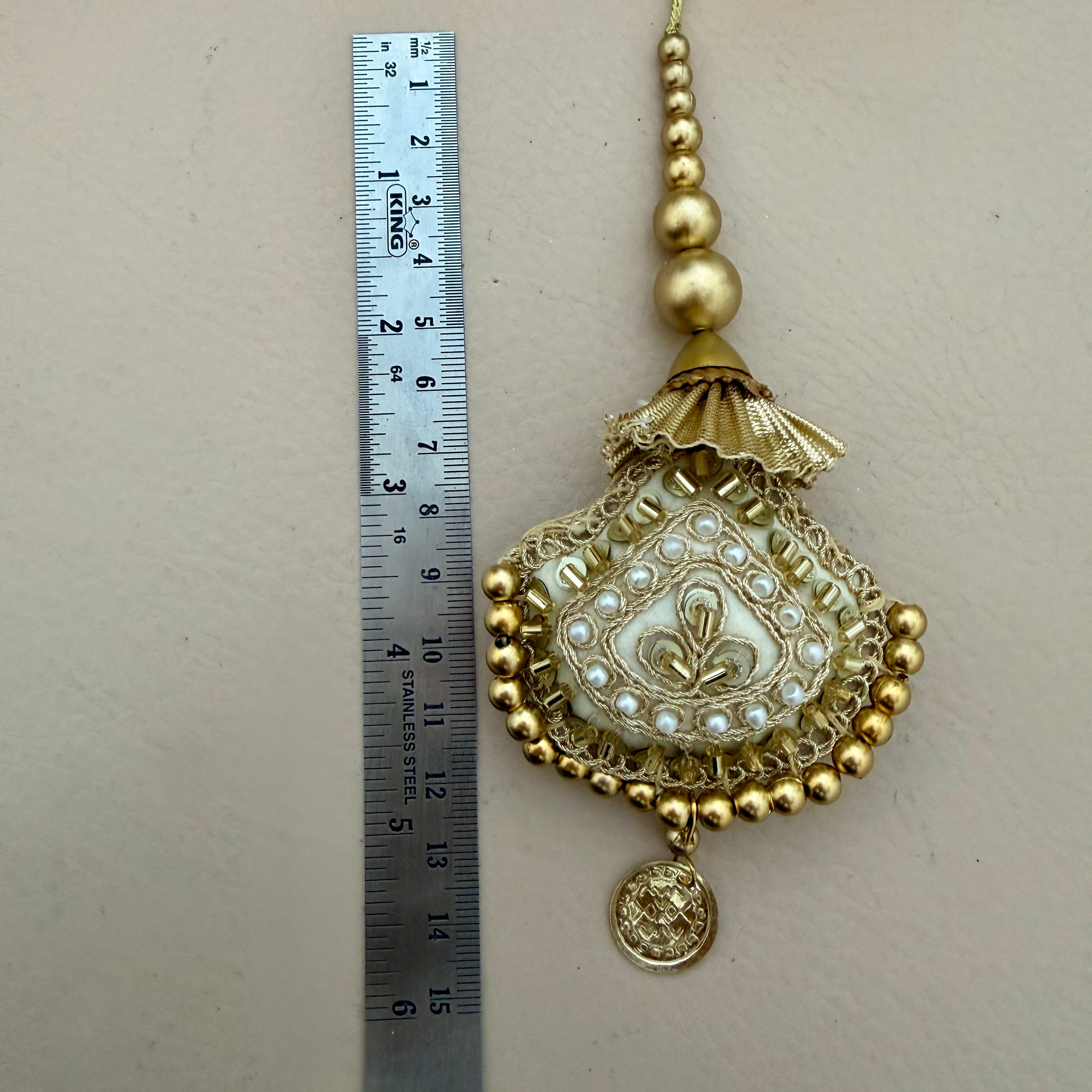 Decorative gold and pearl pendant next to a ruler on a beige background