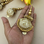 Decorative gold jewelry piece held in a hand with a neutral background