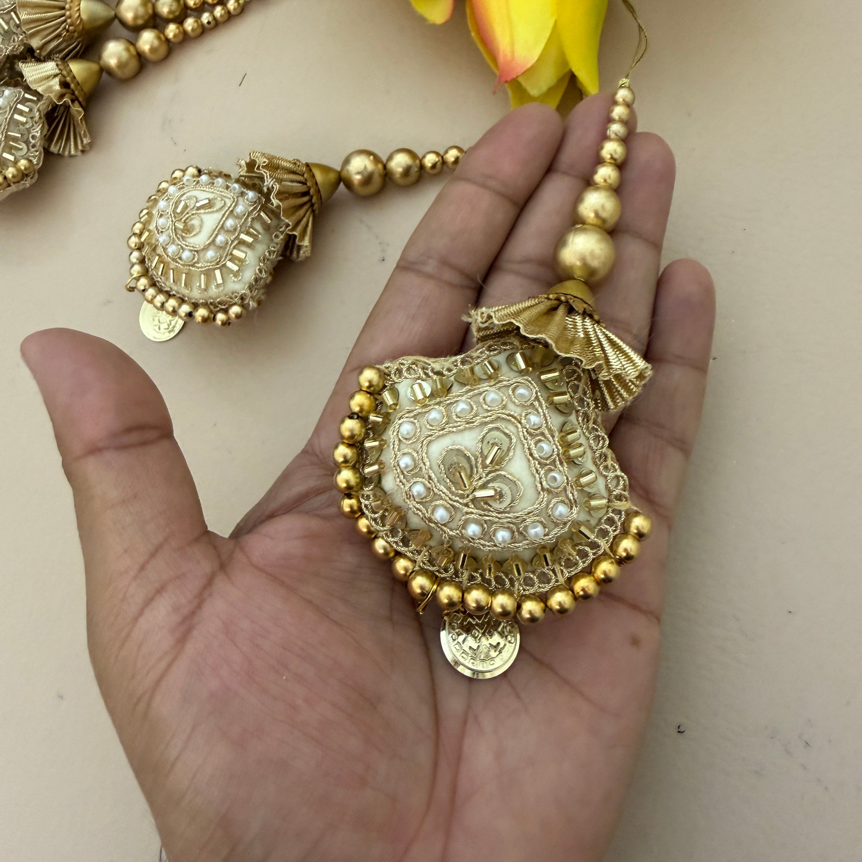 Decorative gold jewelry piece held in a hand with a neutral background