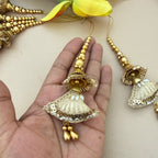 Decorative gold jhumka earrings held in a hand with a light background