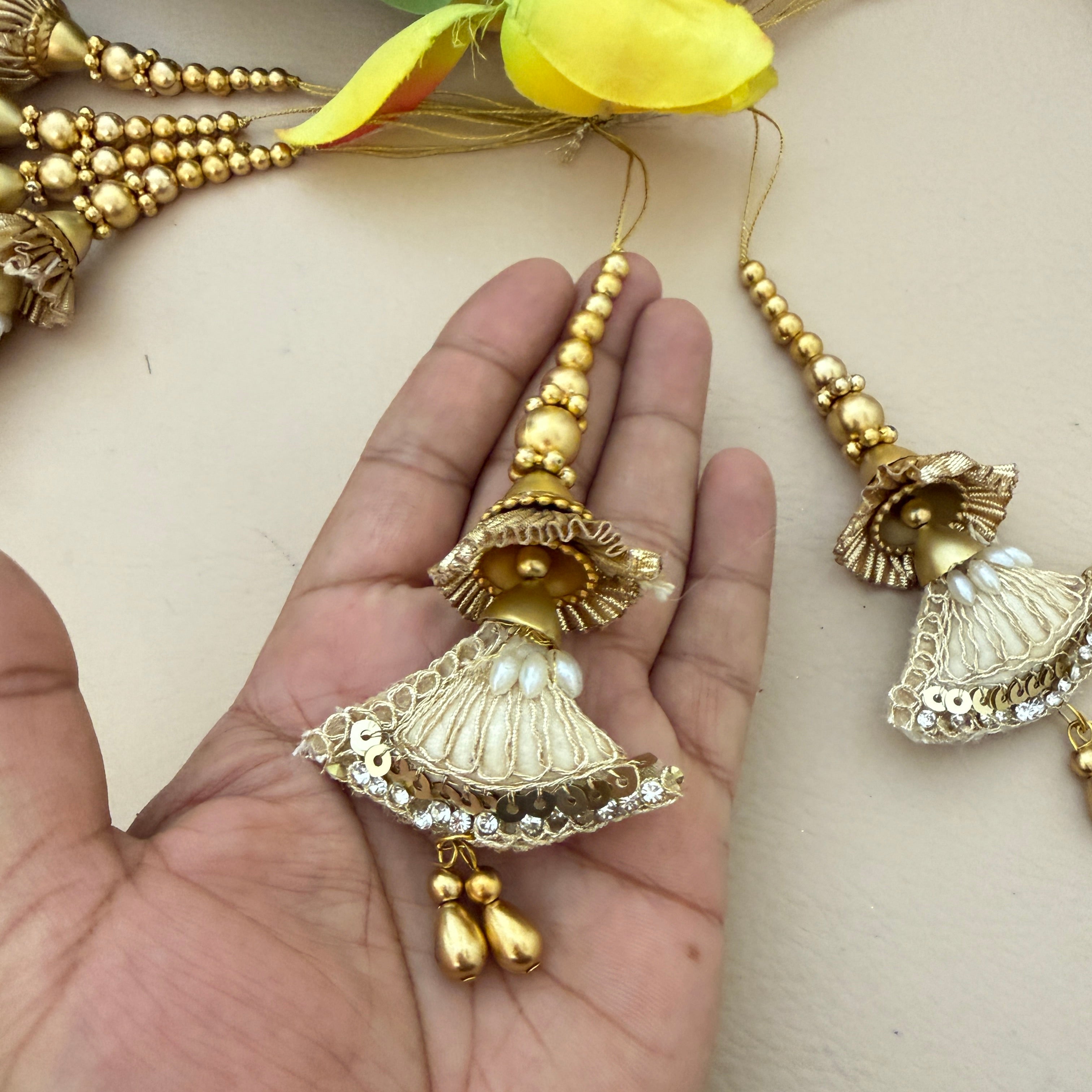 Decorative gold jhumka earrings held in a hand with a light background