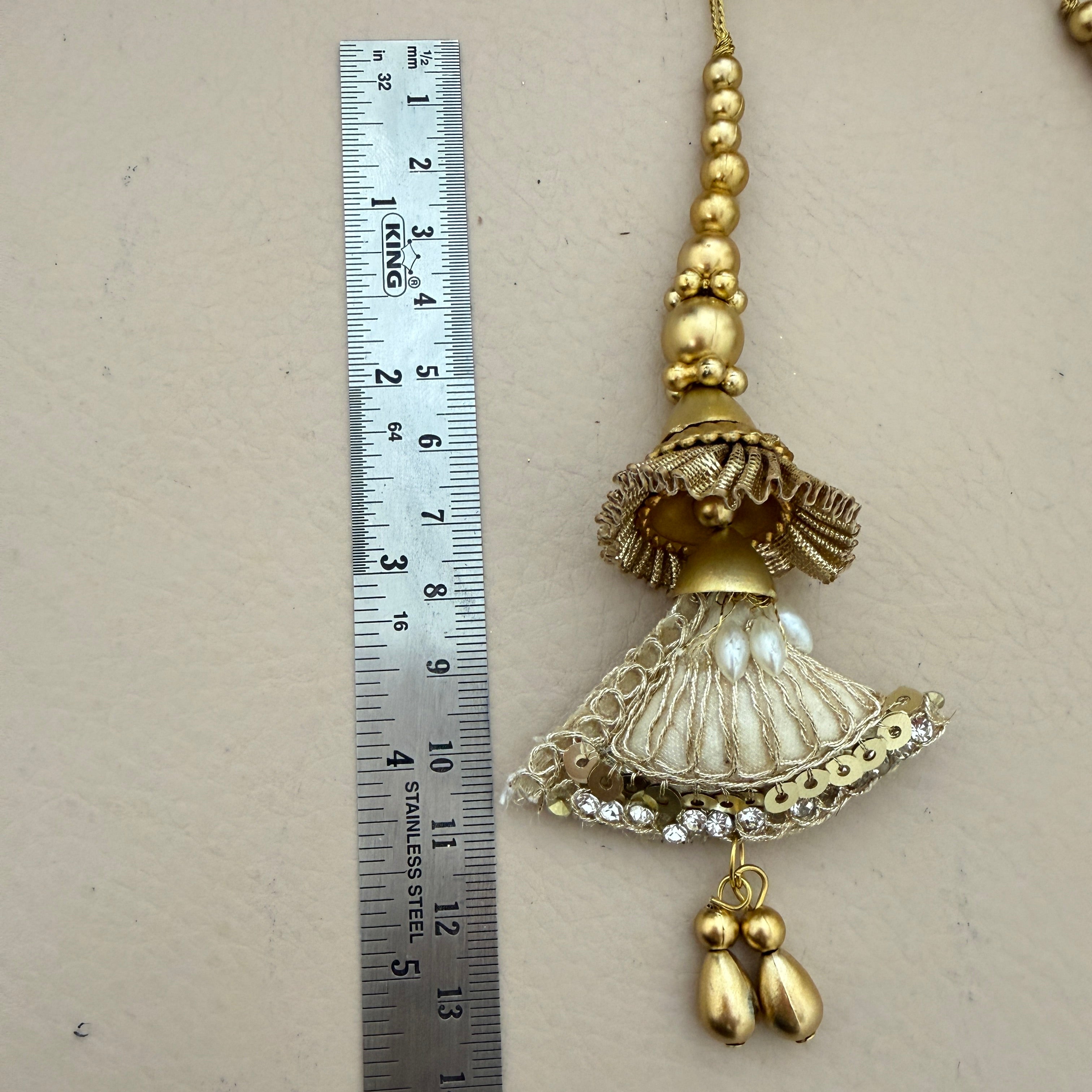 Decorative gold tassel with beads and pearls next to a ruler for scale on a beige background