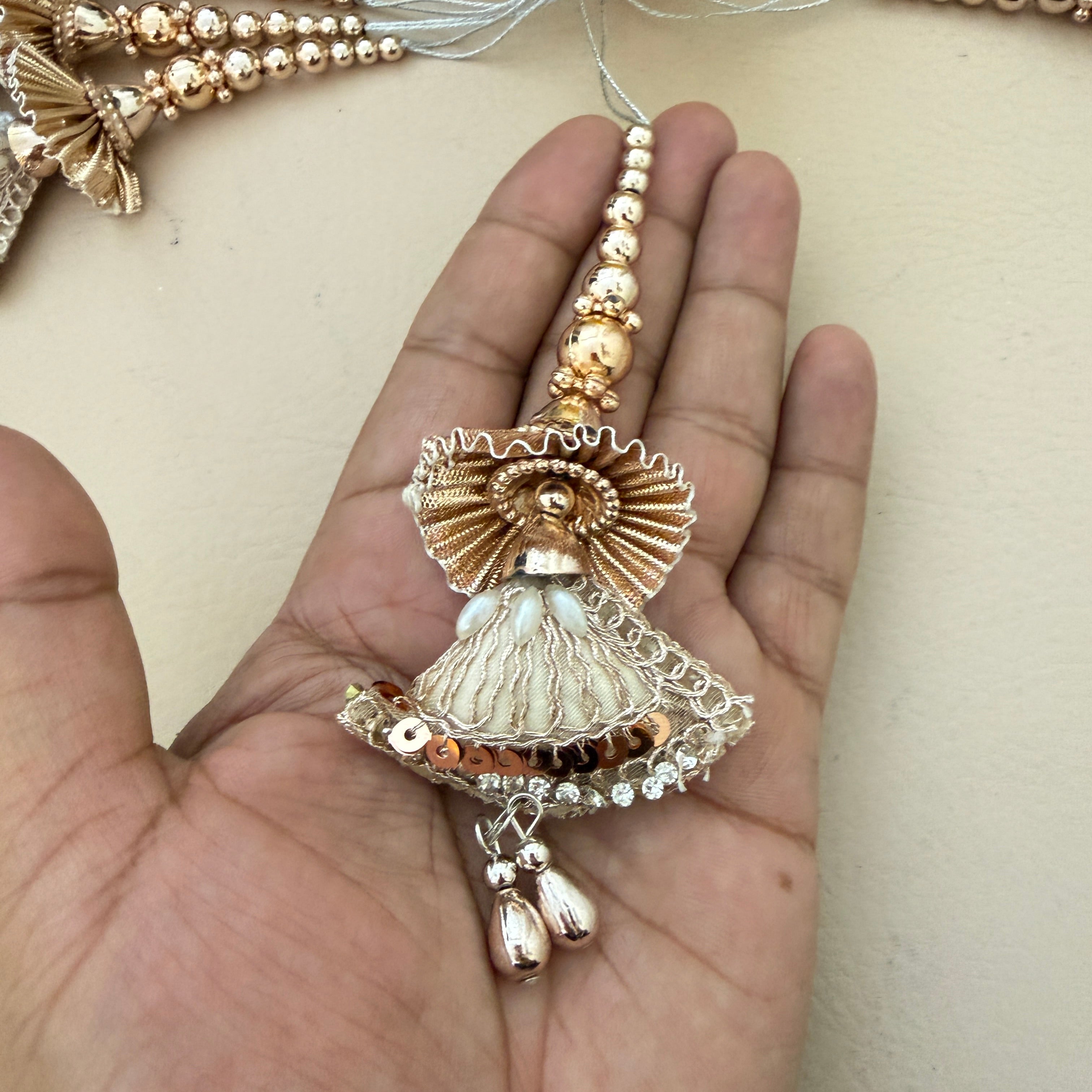 Decorative gold and pearl pendant held in a hand against a neutral background