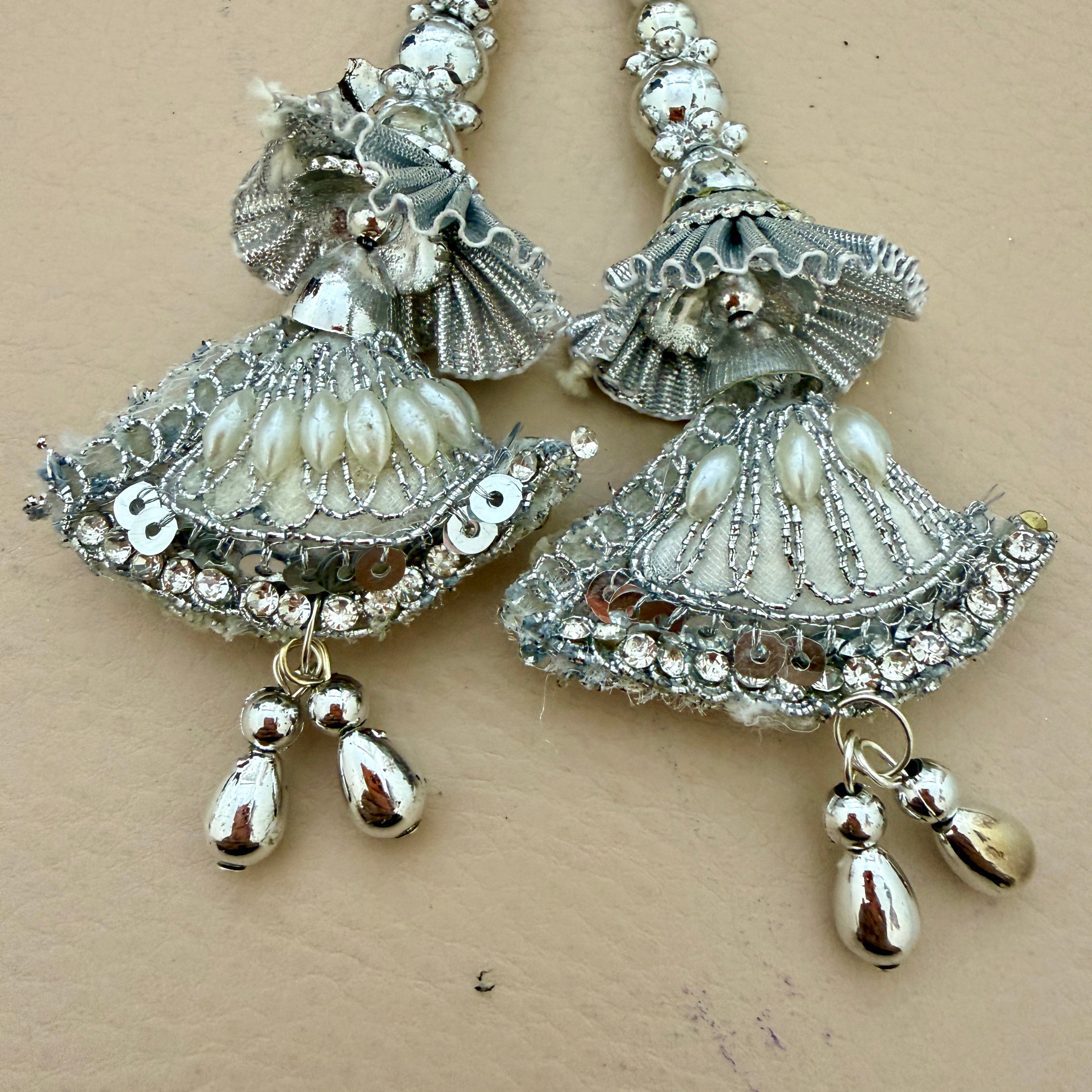 Pair of silver and pearl jhumka earrings on a beige background