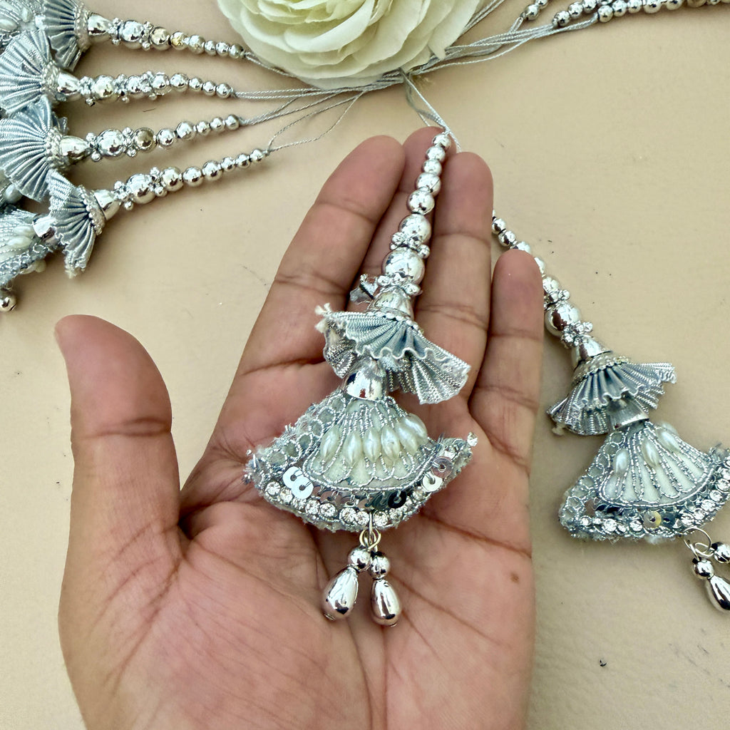 Decorative silver pendant held in a hand with more pendants on a beige background