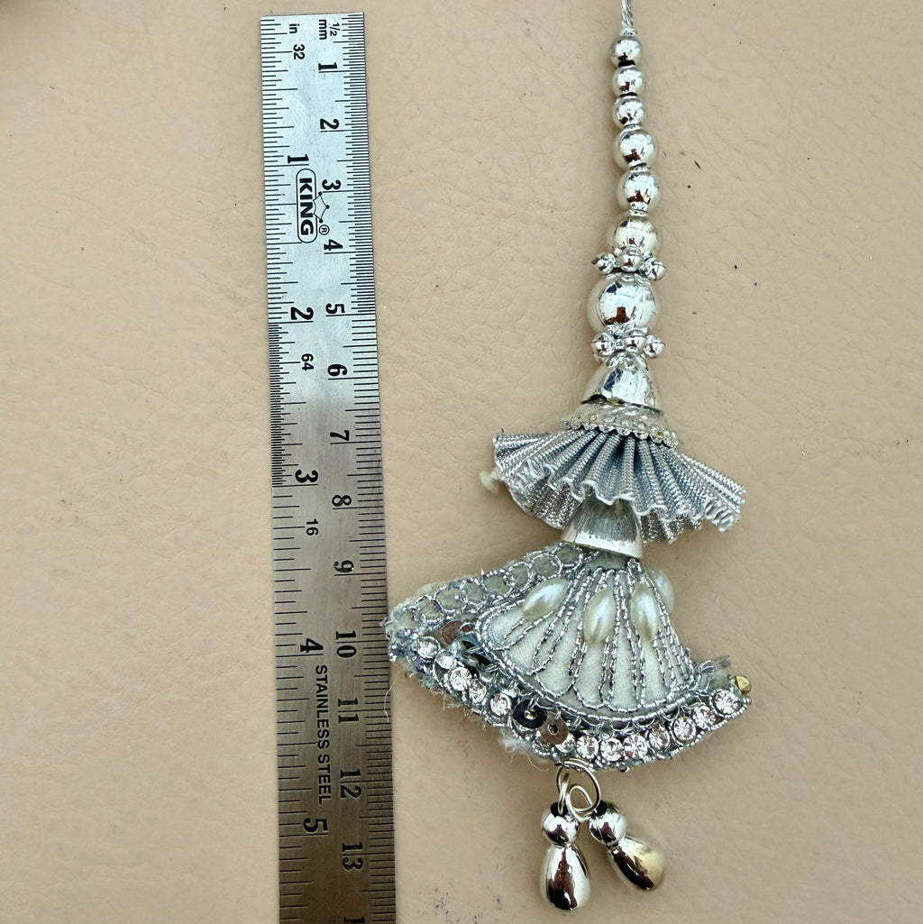 Decorative silver hanging ornament next to a ruler on a beige background