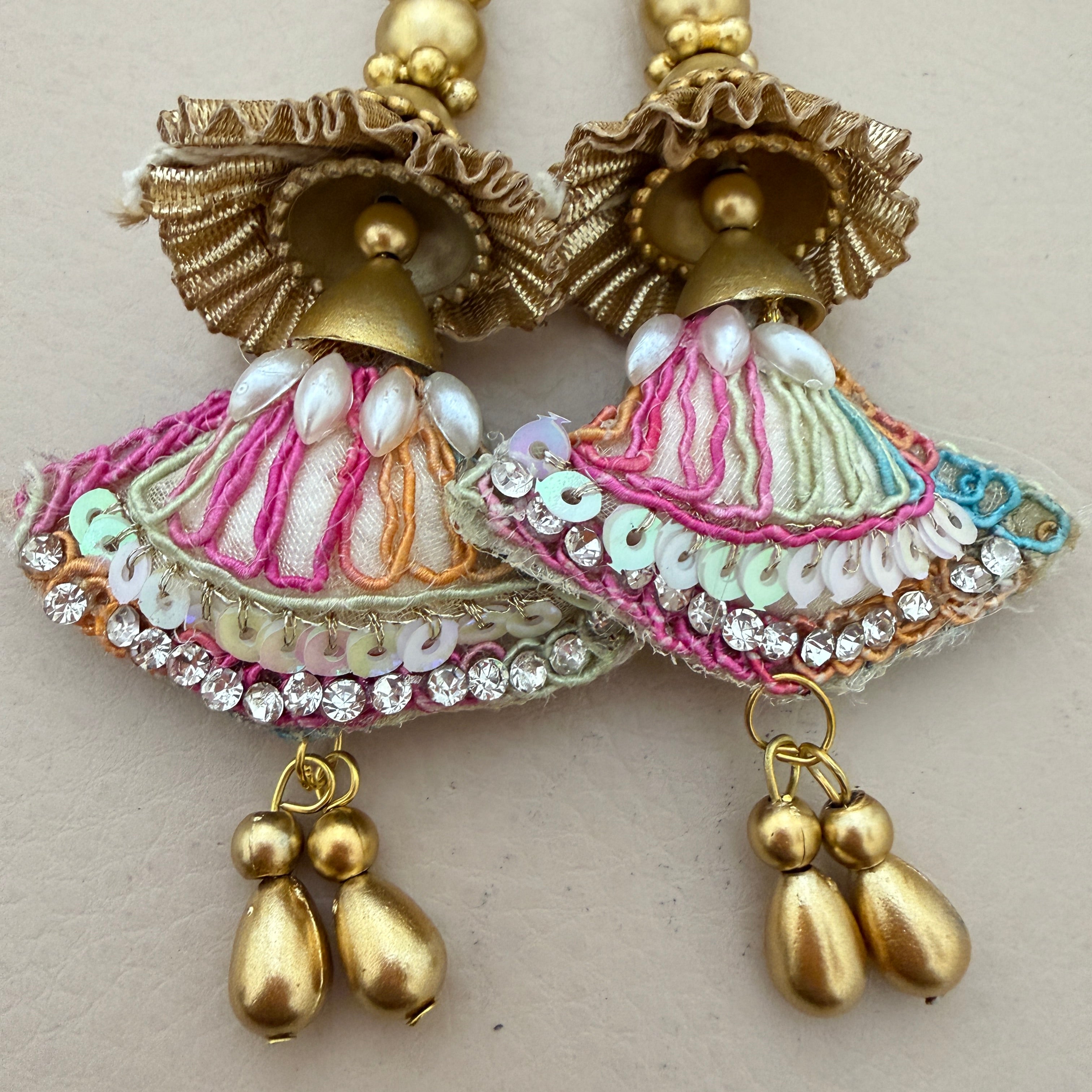 Decorative earrings with gold, pink, and white details on a light background