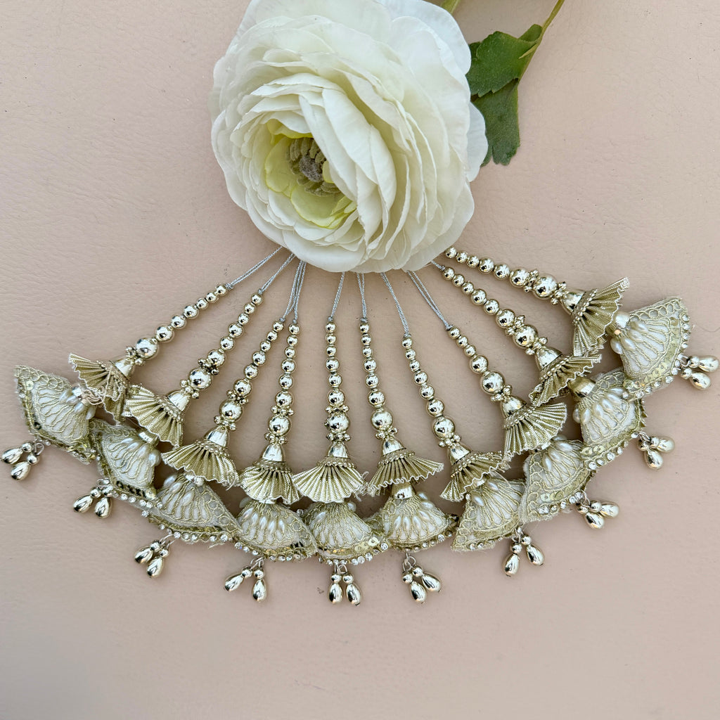 Decorative headpiece with shell-like designs and beads on a light pink background with a white flower.