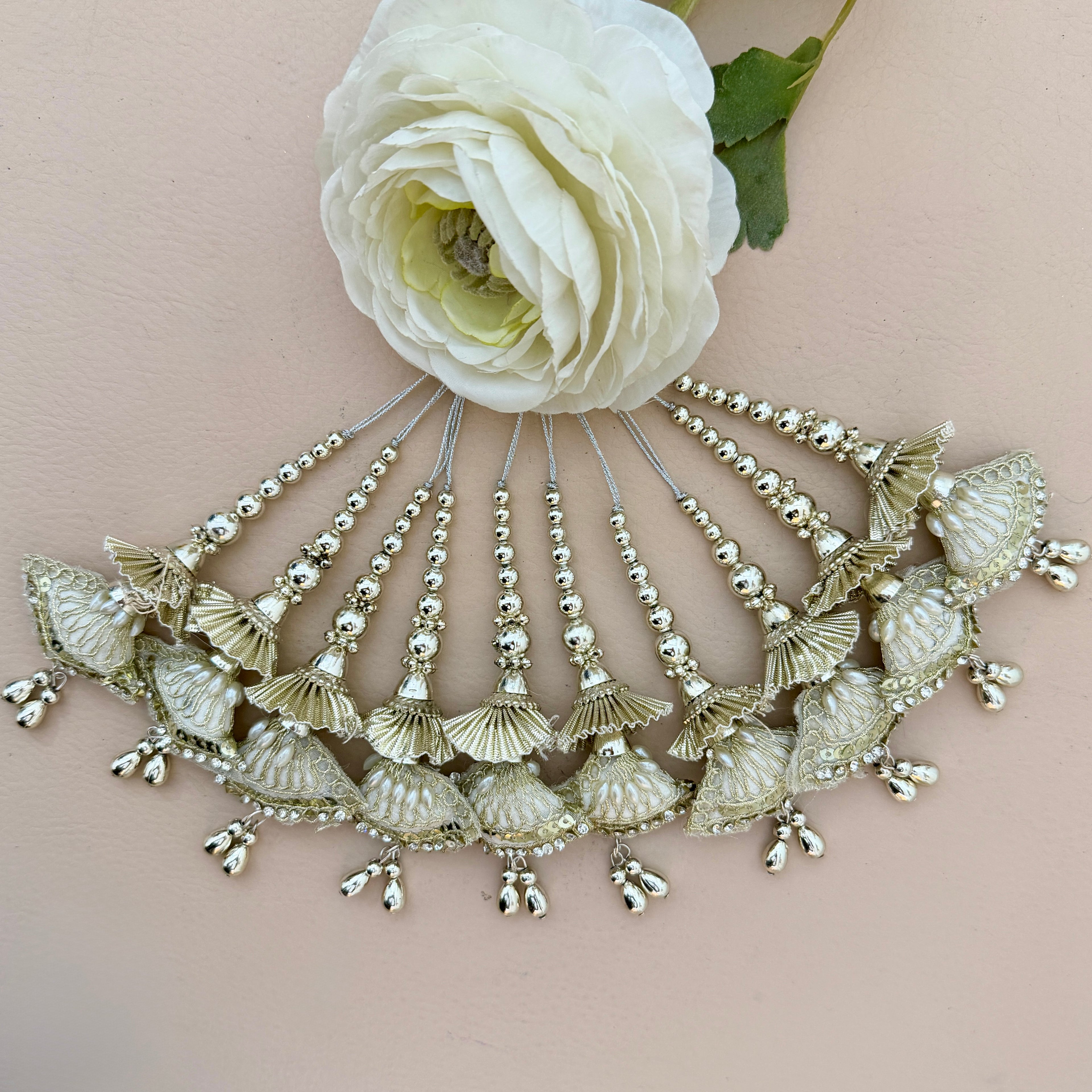 Decorative headpiece with shell-like designs and beads on a light pink background with a white flower.