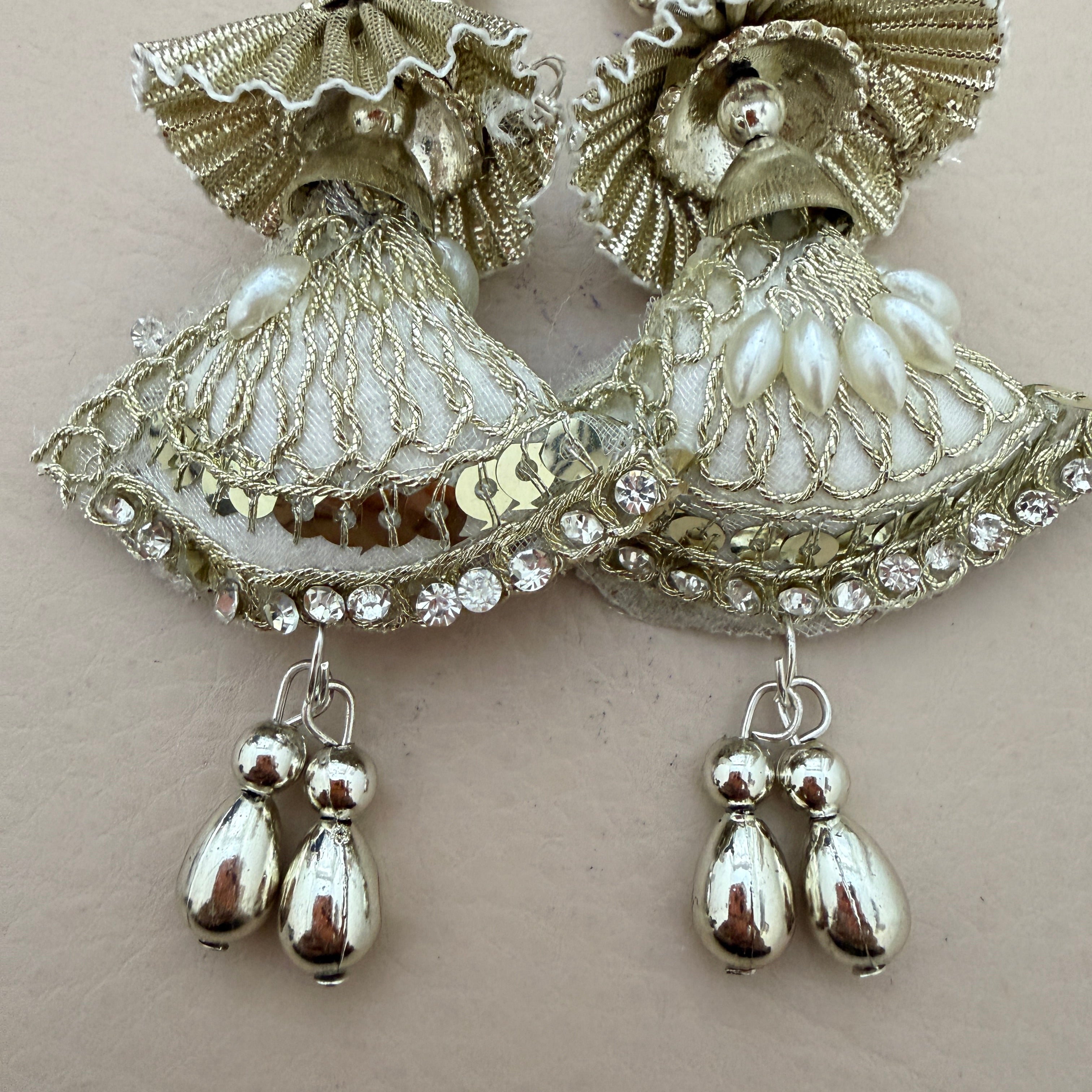 Silver earrings with intricate designs and pearl-like beads on a light background