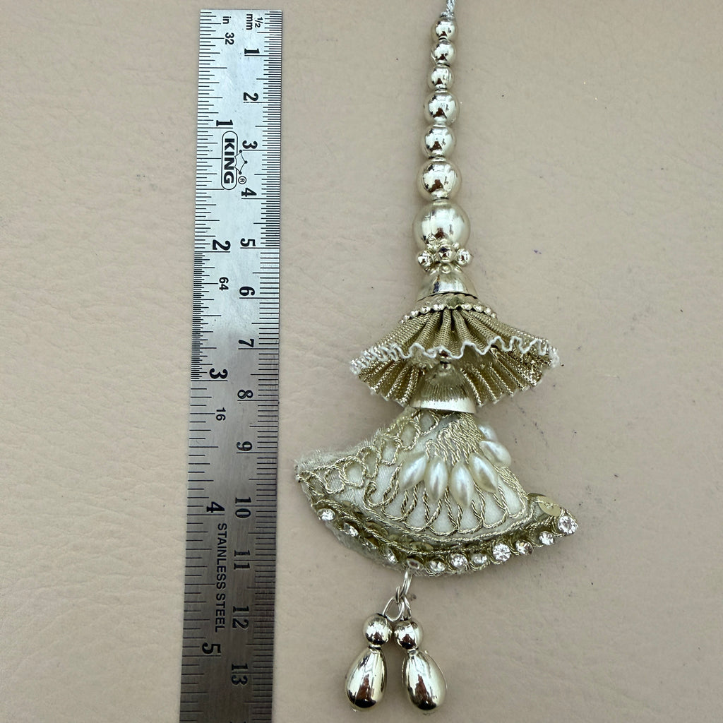Decorative silver jhumka earring with a ruler for scale on a beige background