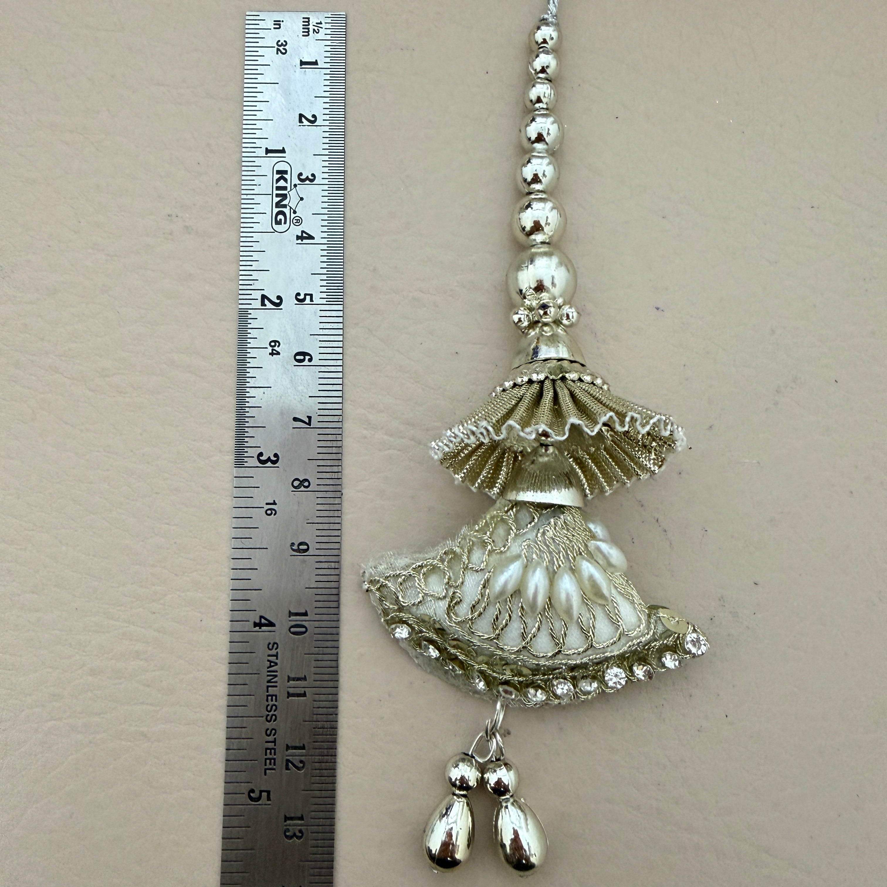 Decorative silver jhumka earring with a ruler for scale on a beige background