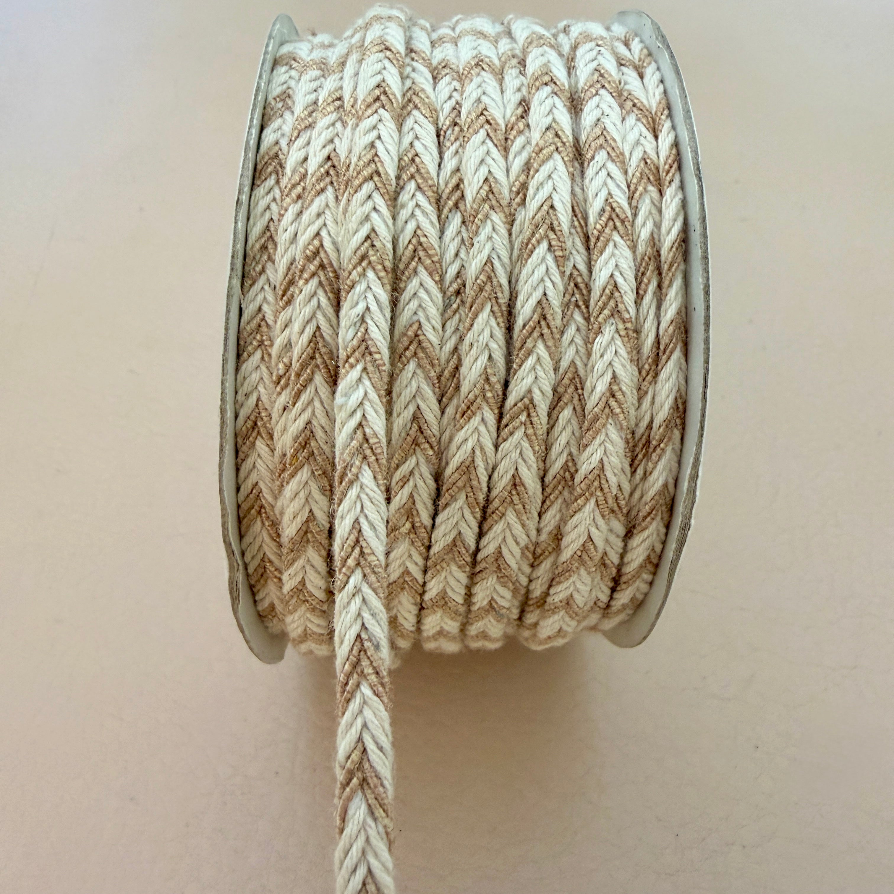 Spool of brown and beige braided cord on a plain background