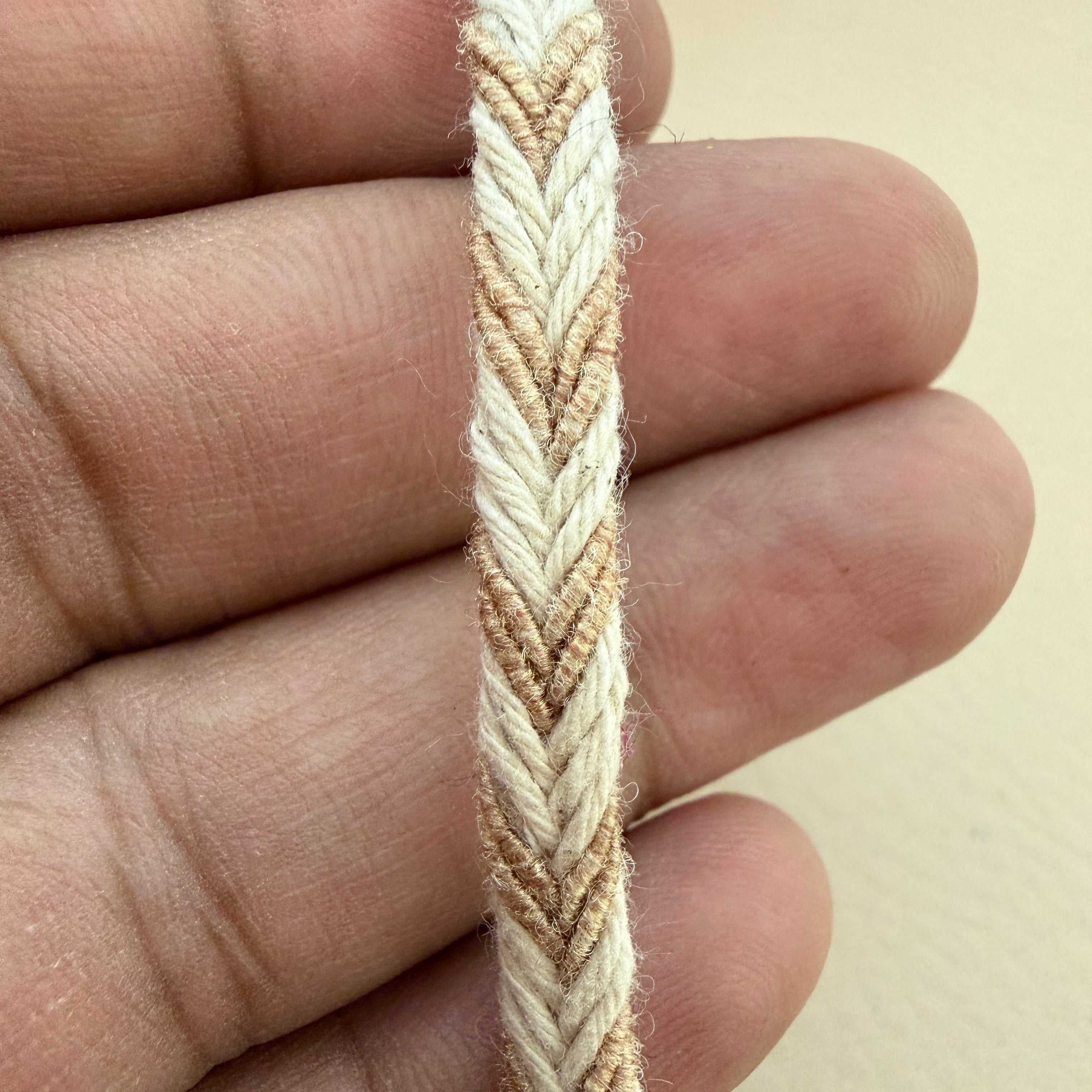 Close-up of a hand holding a braided beige and white cord.