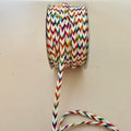 Spool of colorful zigzag-patterned rope on a beige background