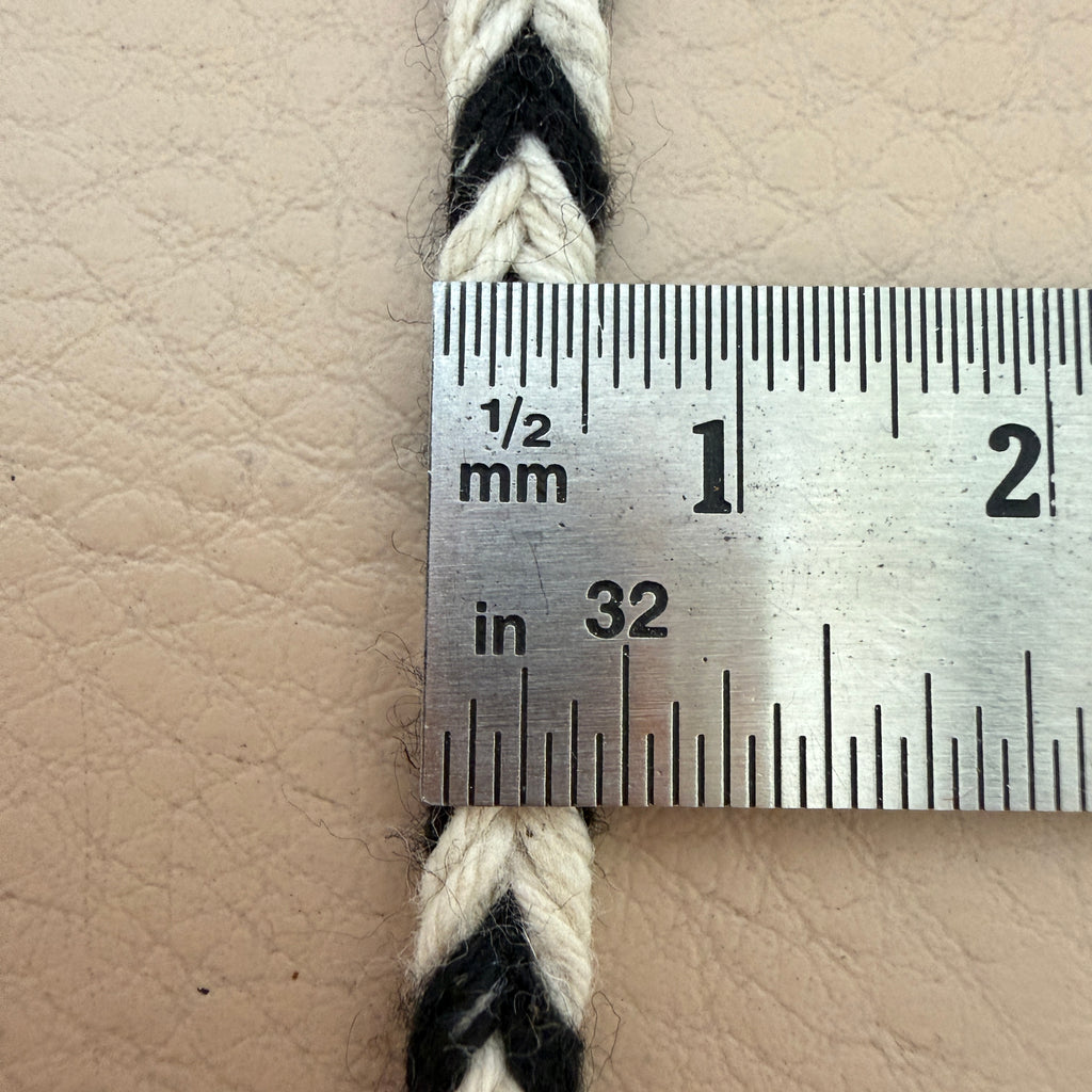 Close-up of a braided cord with a ruler showing measurements on a beige leather surface