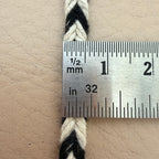 Close-up of a braided cord with a ruler showing measurements on a beige leather surface