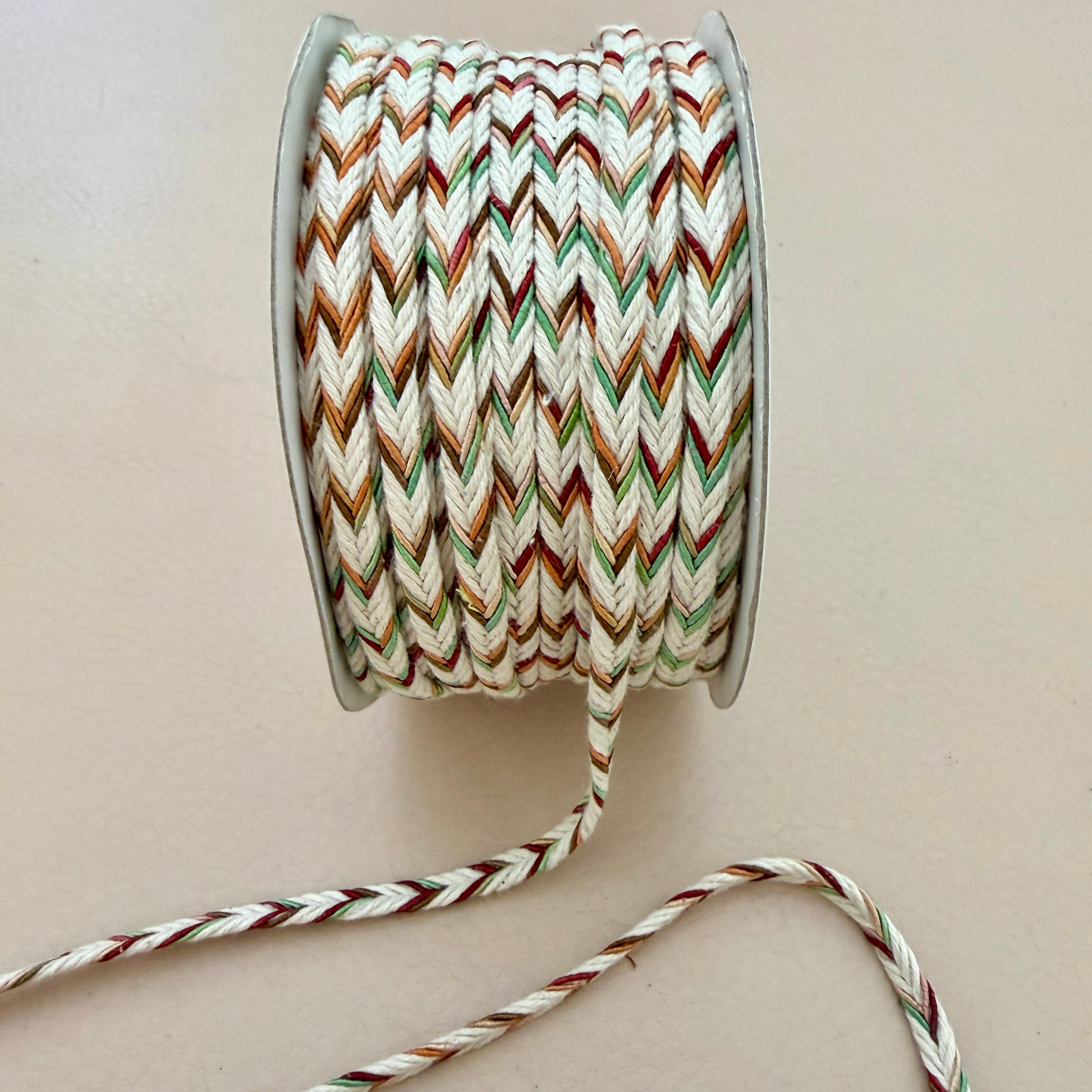 Spool of multicolored braided cable on a beige background