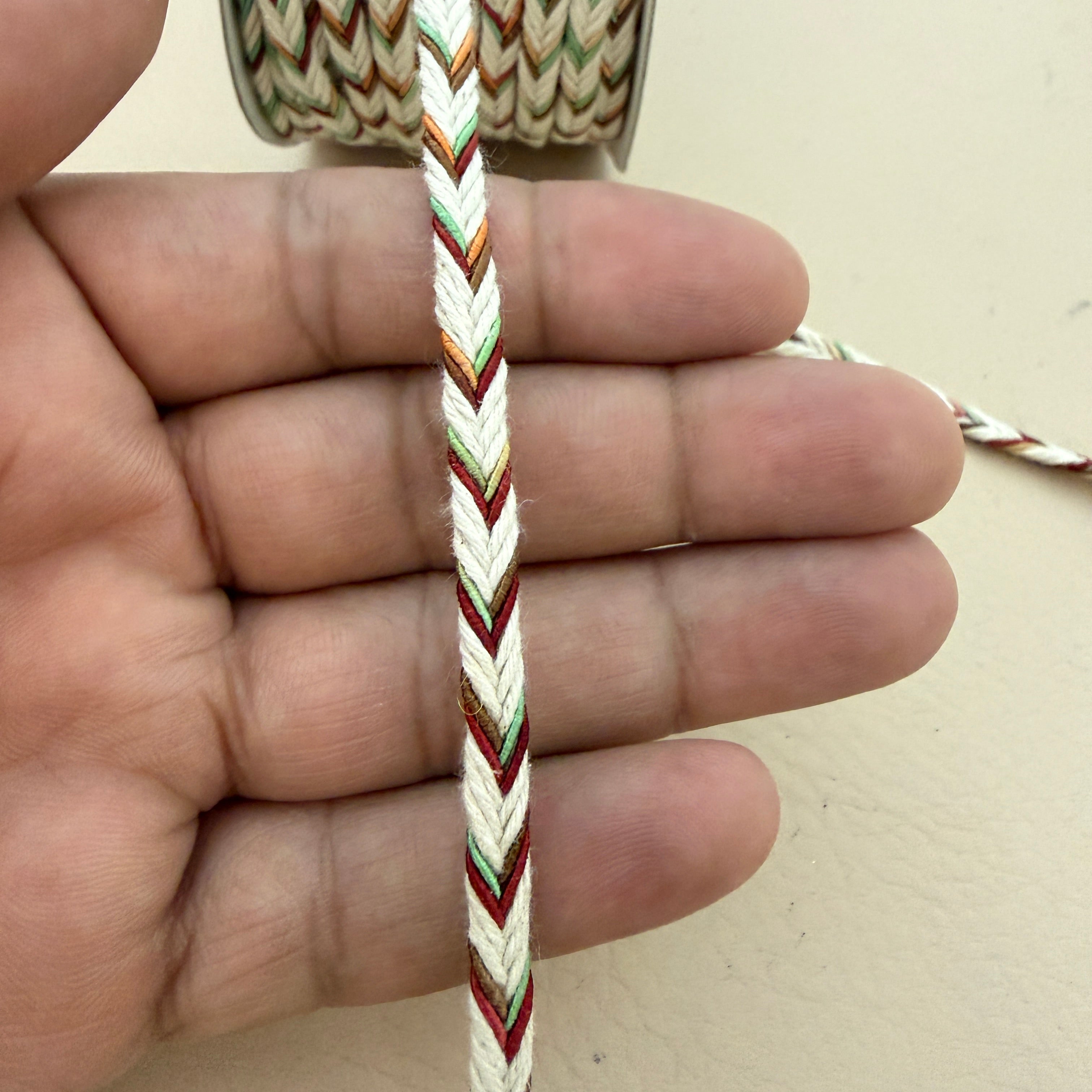 Hand holding a multicolored braided cord against a neutral background