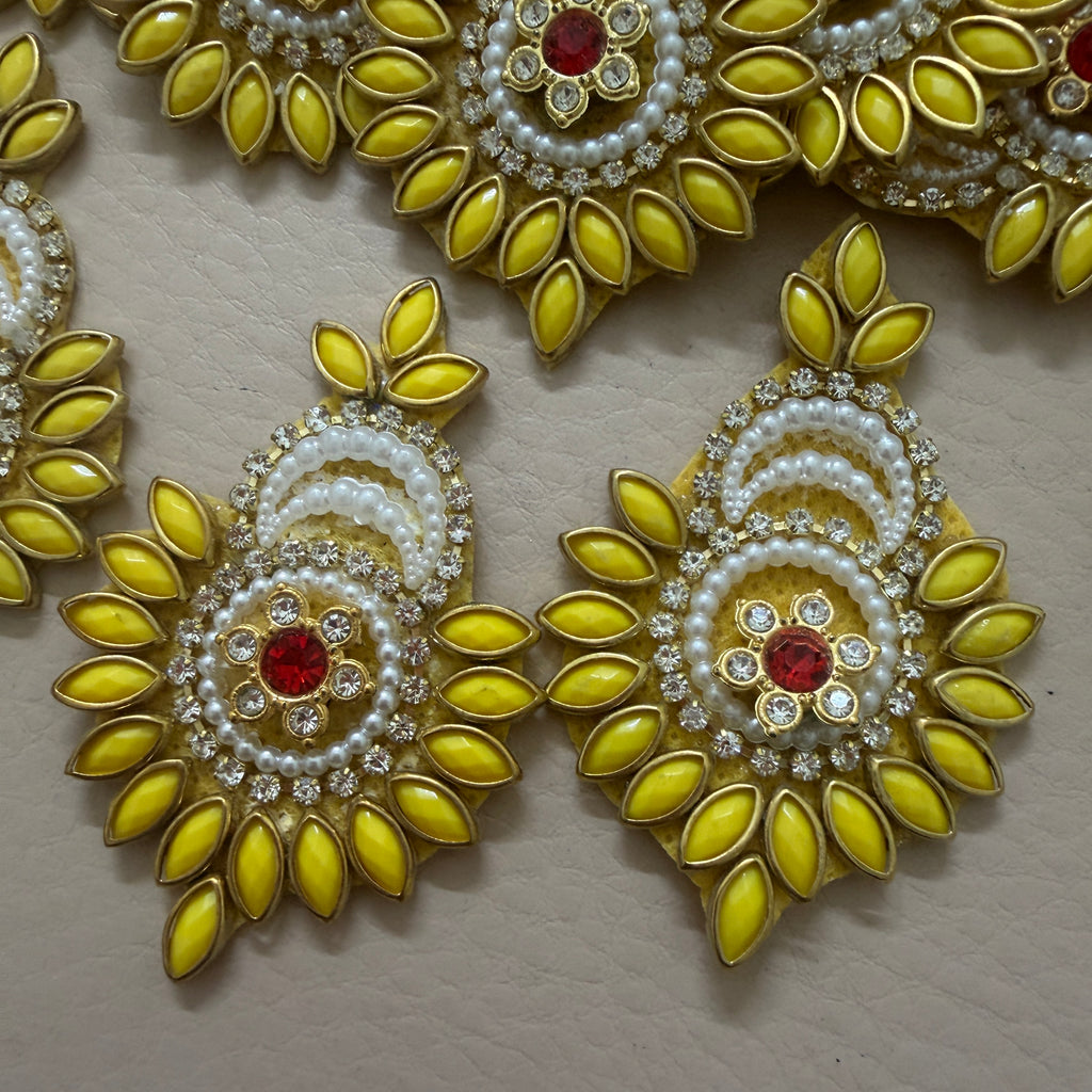 Decorative earrings with yellow leaves, white pearls, and red stones on a beige background