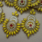 Decorative earrings with yellow leaves, white pearls, and red stones on a beige background