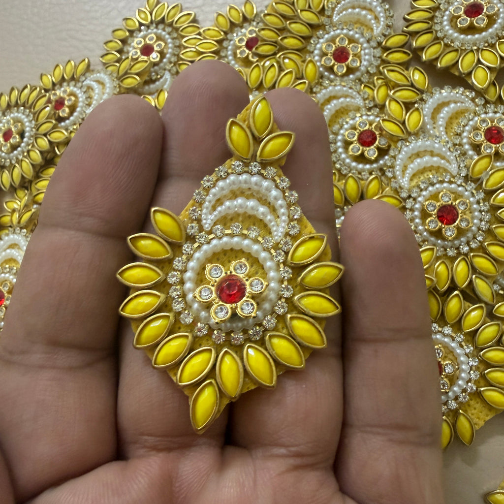 Decorative gold and yellow earring held between fingers with a patterned background