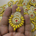 Decorative gold and yellow earring held between fingers with a patterned background
