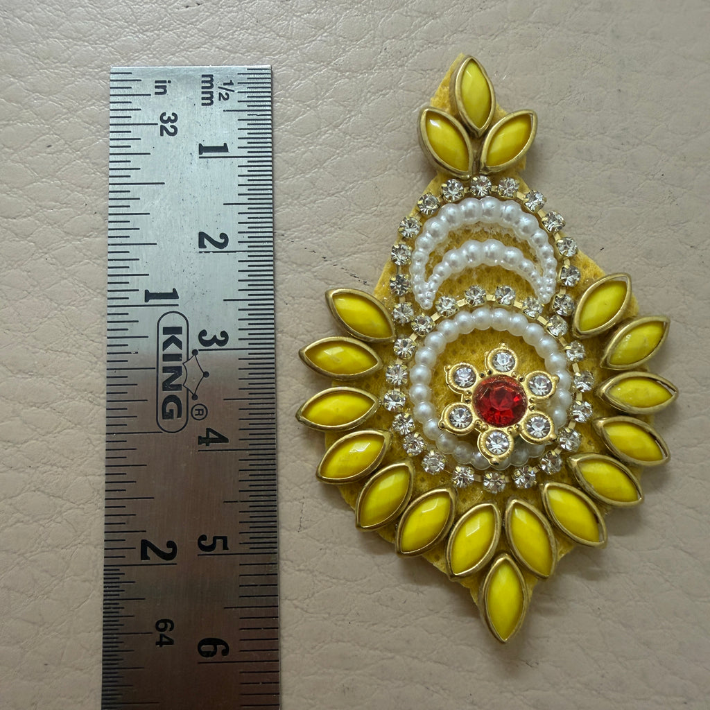 Decorative yellow and gold brooch with red gemstone next to a ruler for scale on a beige background