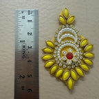 Decorative yellow and gold brooch with red gemstone next to a ruler for scale on a beige background