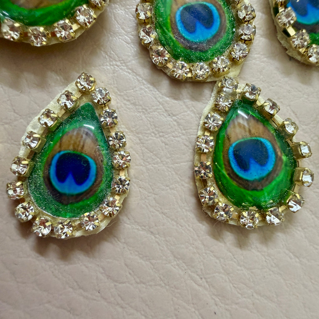Peacock feather design buttons with rhinestone accents on a beige background