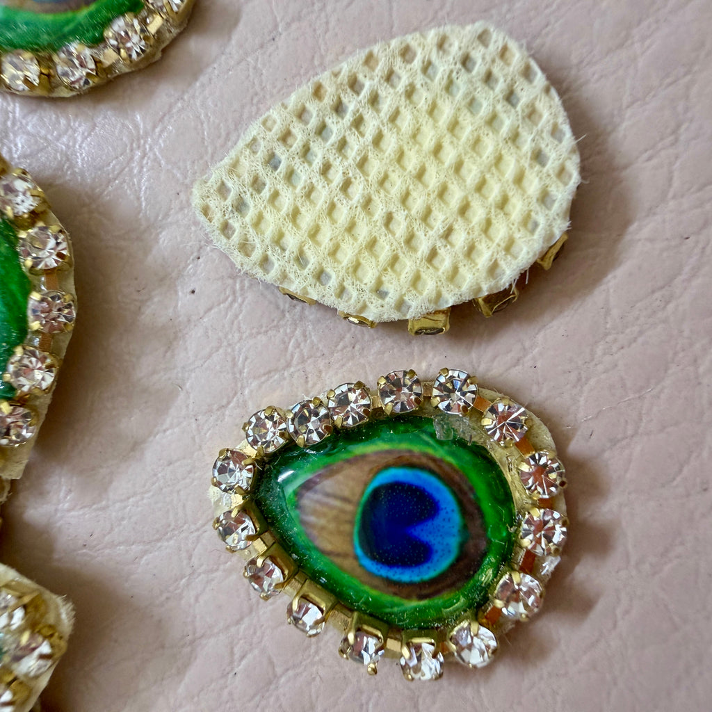 Decorative peacock feather button with rhinestones on a textured surface