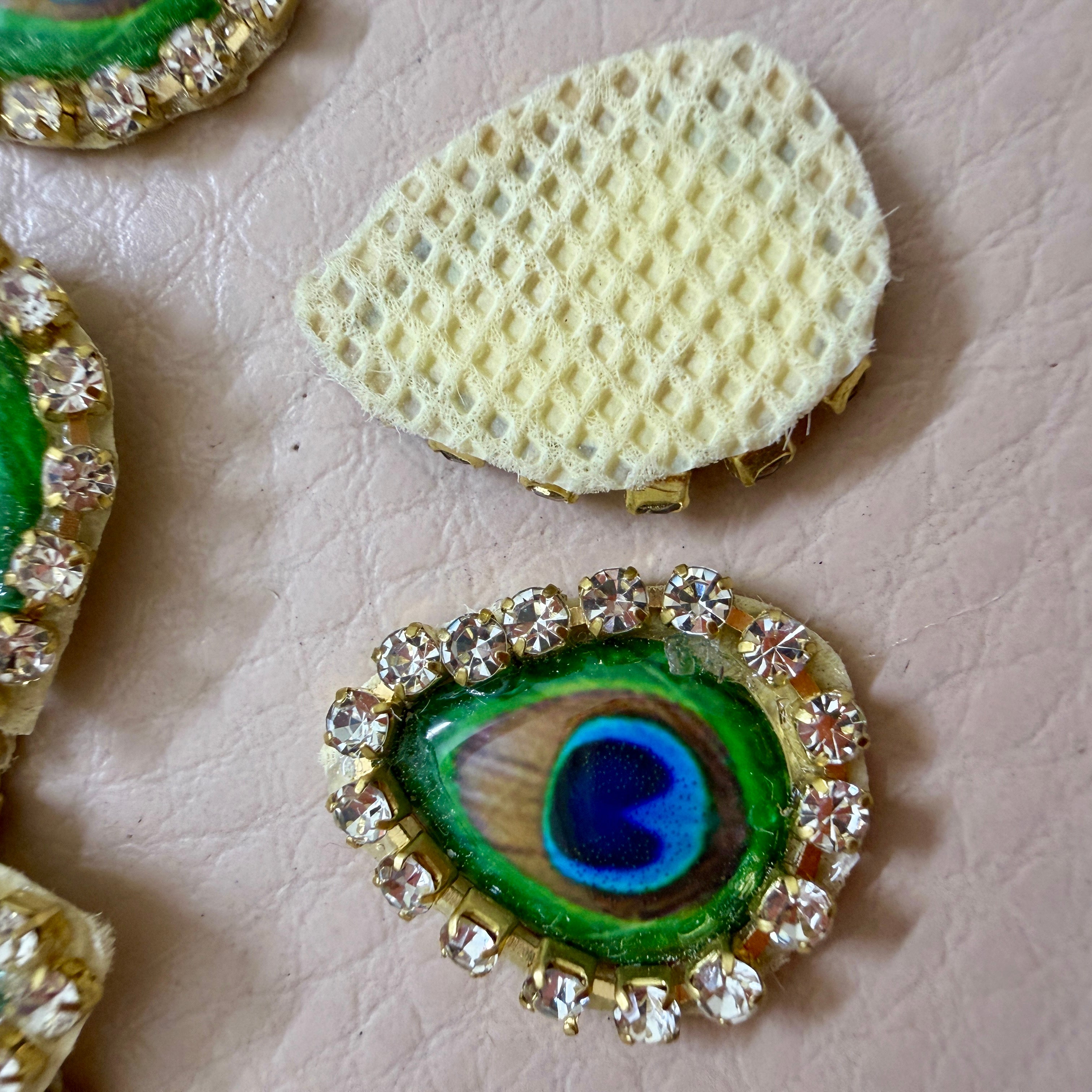 Decorative peacock feather button with rhinestones on a textured surface