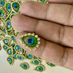 Close-up of a hand holding a decorative peacock feather design on fabric.